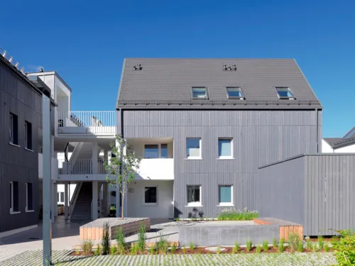 Blick von außen auf ein modernes Gebäude mit Holzfassade und mehreren Wohneinheiten.